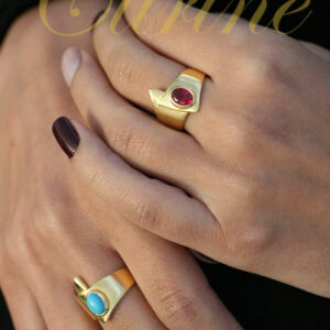 Two gold rings with red and turquoise cabochon stones worn on hand